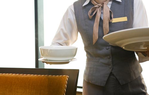 A standing waitress holding a cup and plate in a restaurant.